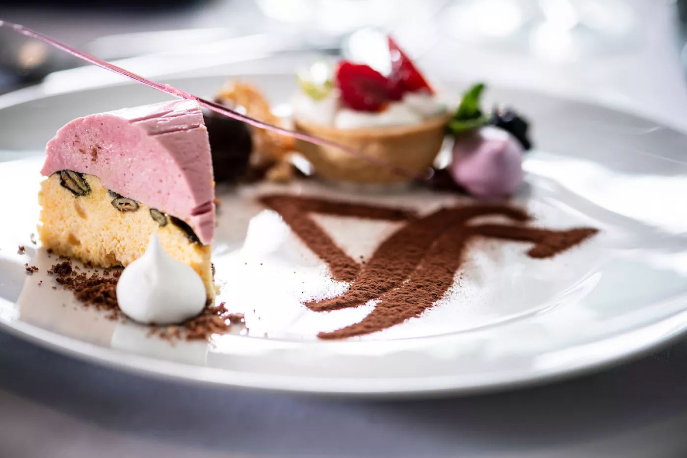A plated dessert of pink berry mousse, meringue kiss, berry tart and cocoa dust
